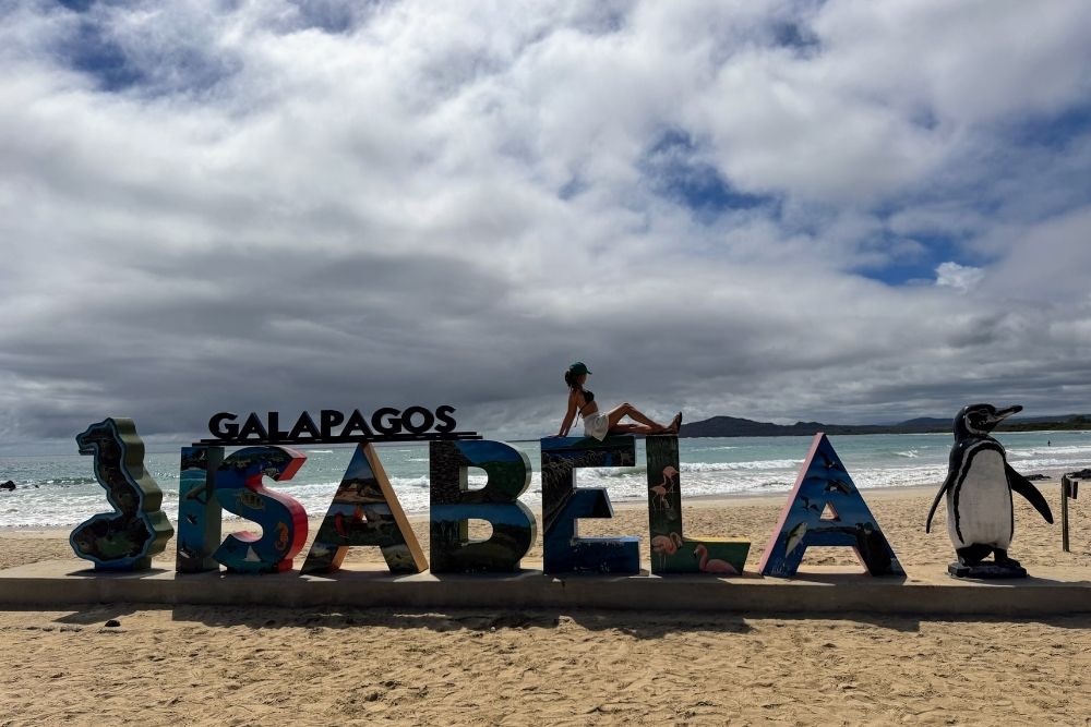 isabela island galapagos traveler relaxing on the isabela sign by the beach, highlighting what to do on isabela island in the galapagos.
